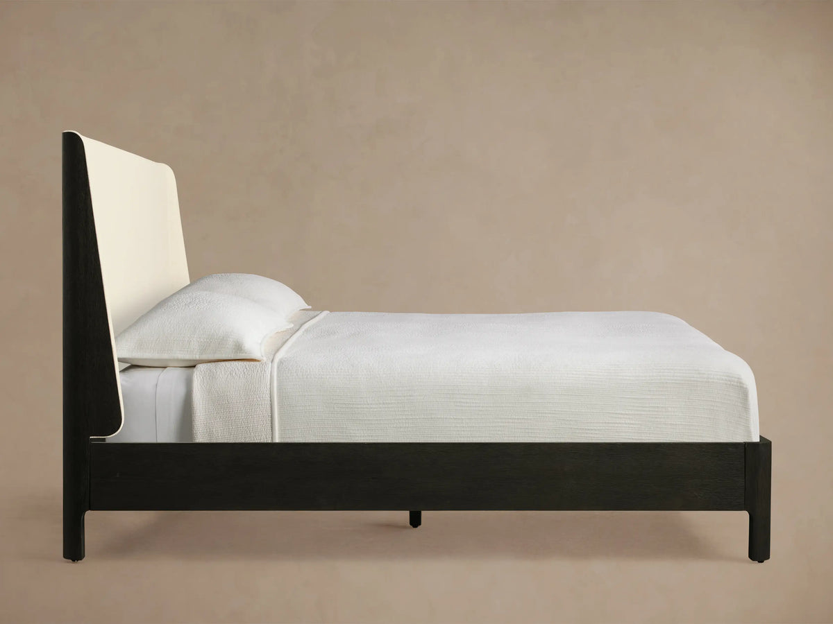 Close-up of Calista Bed headboard's rounded corner, showing a dark oak veneer frame and light cream textured fabric upholstery.