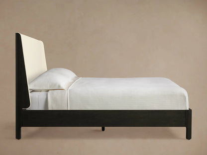 Close-up of Calista Bed headboard's rounded corner, showing a dark oak veneer frame and light cream textured fabric upholstery.