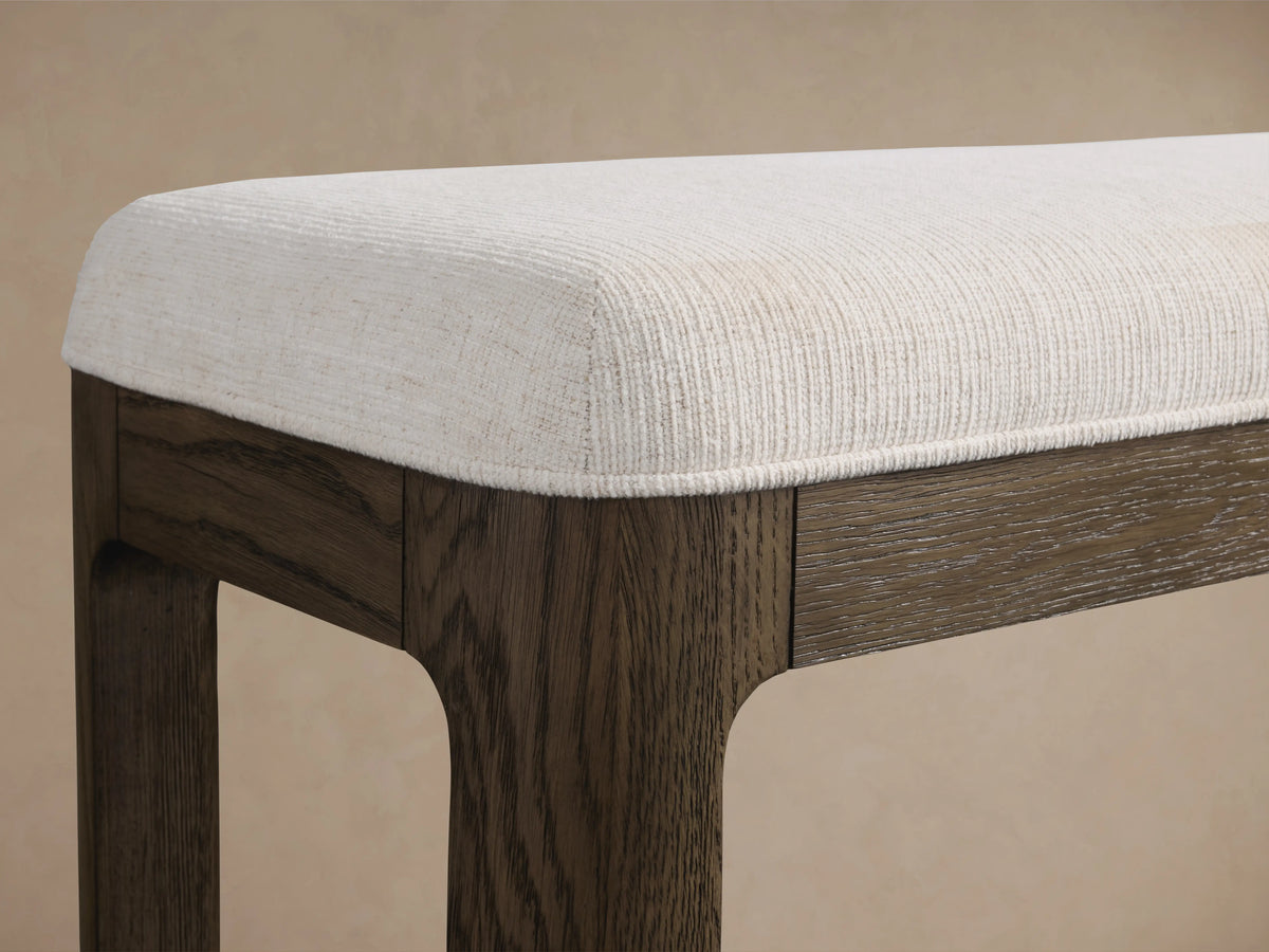Calista Bench featuring a veneered oak frame with hand-applied finishes and a white cushioned seat, on a wood floor.