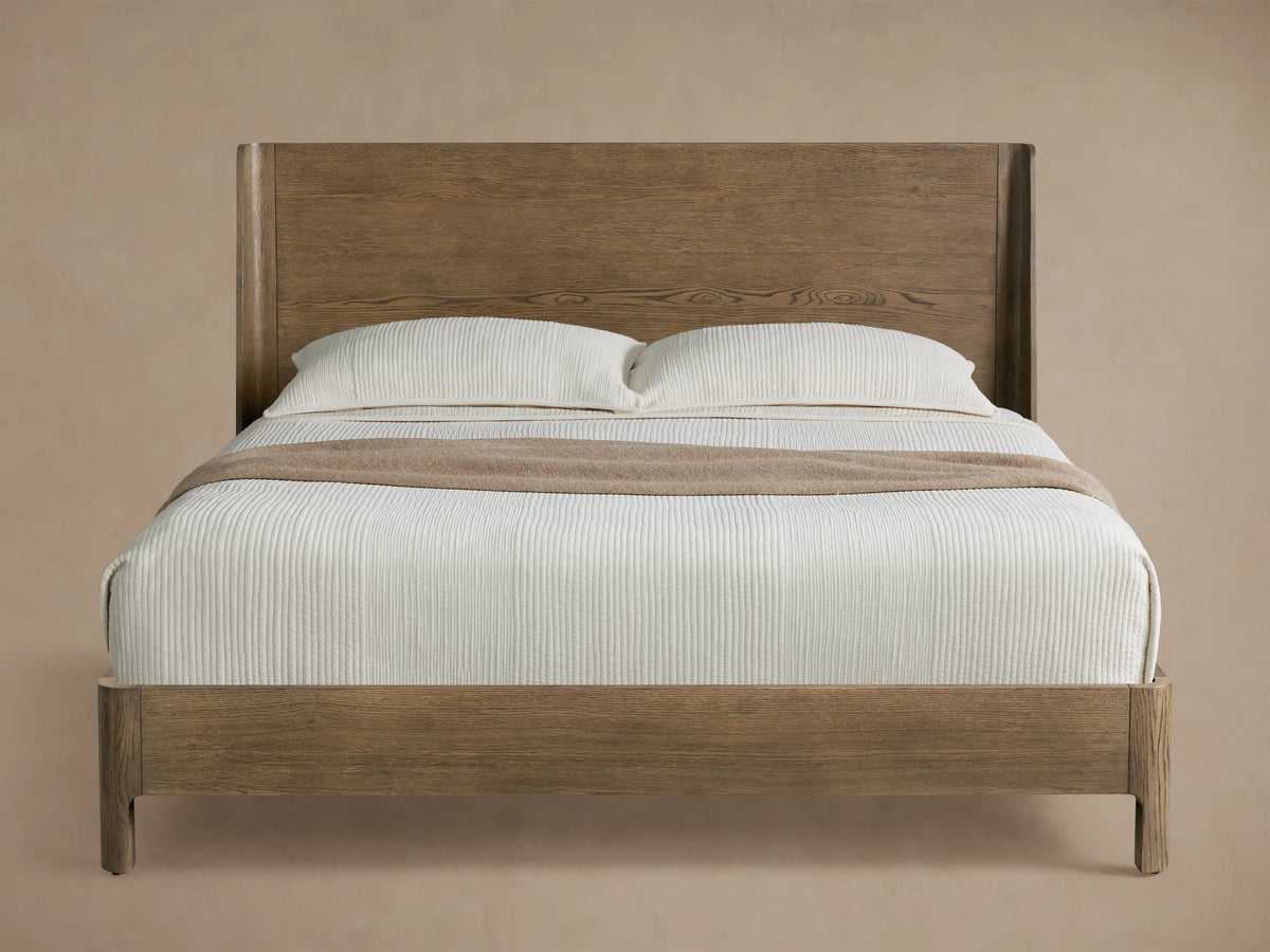 Calista Wood Bed with light brown veneered oak frame and high tapered headboard, dressed in white bedding & tan throw.