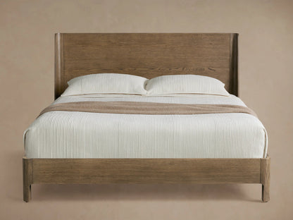 Calista Wood Bed with light brown veneered oak frame and high tapered headboard, dressed in white bedding & tan throw.