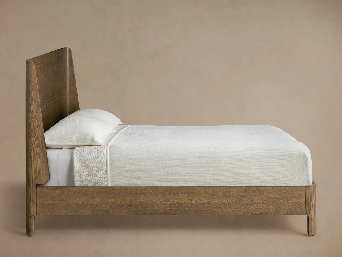 Close-up of Calista Wood Bed's dark brown veneered oak corner, showing rich wood grain and a smoothly curved edge.