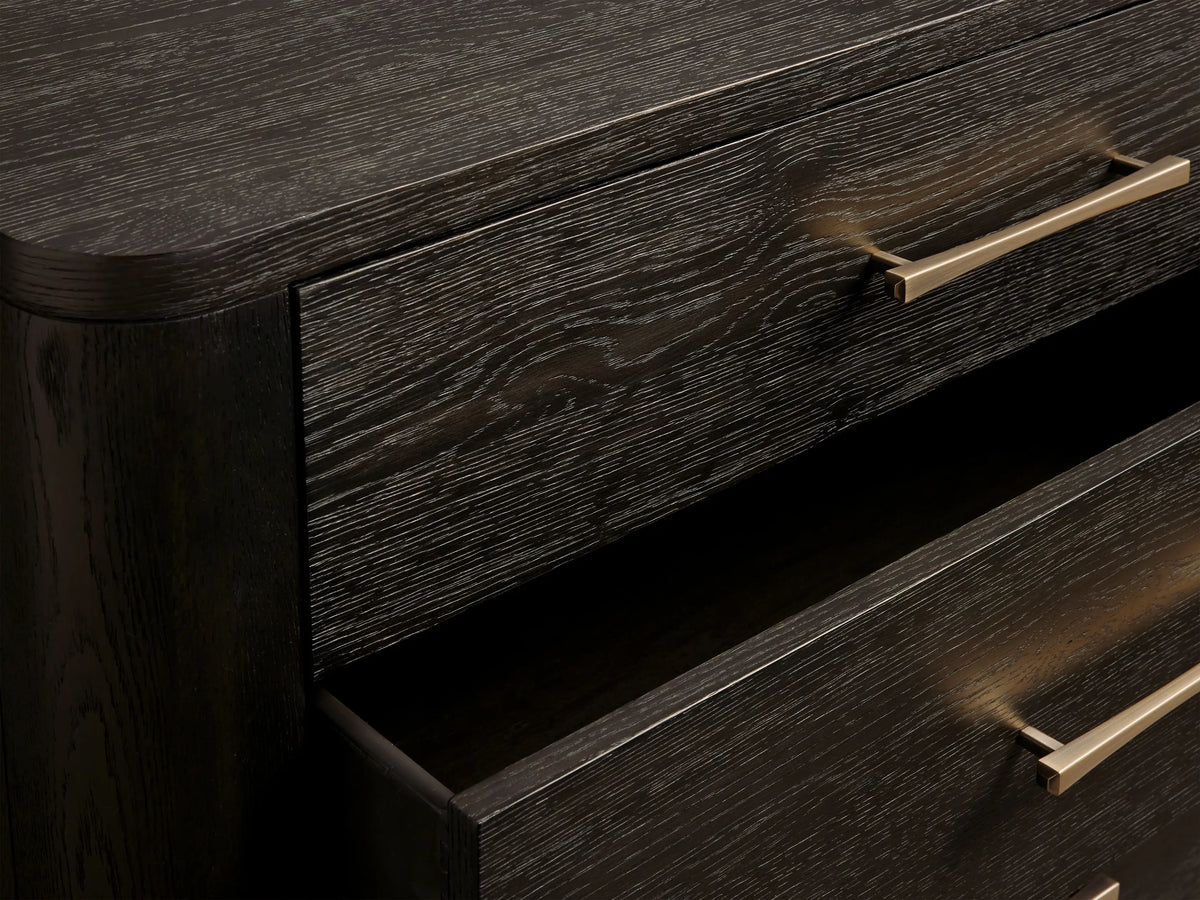 Calista Three-Drawer Chest. Dark brown oak with visible grain, rounded edges. Three drawers with sleek gold bar handles on a wood floor.