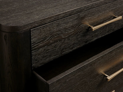 Calista Three-Drawer Chest. Dark brown oak with visible grain, rounded edges. Three drawers with sleek gold bar handles on a wood floor.