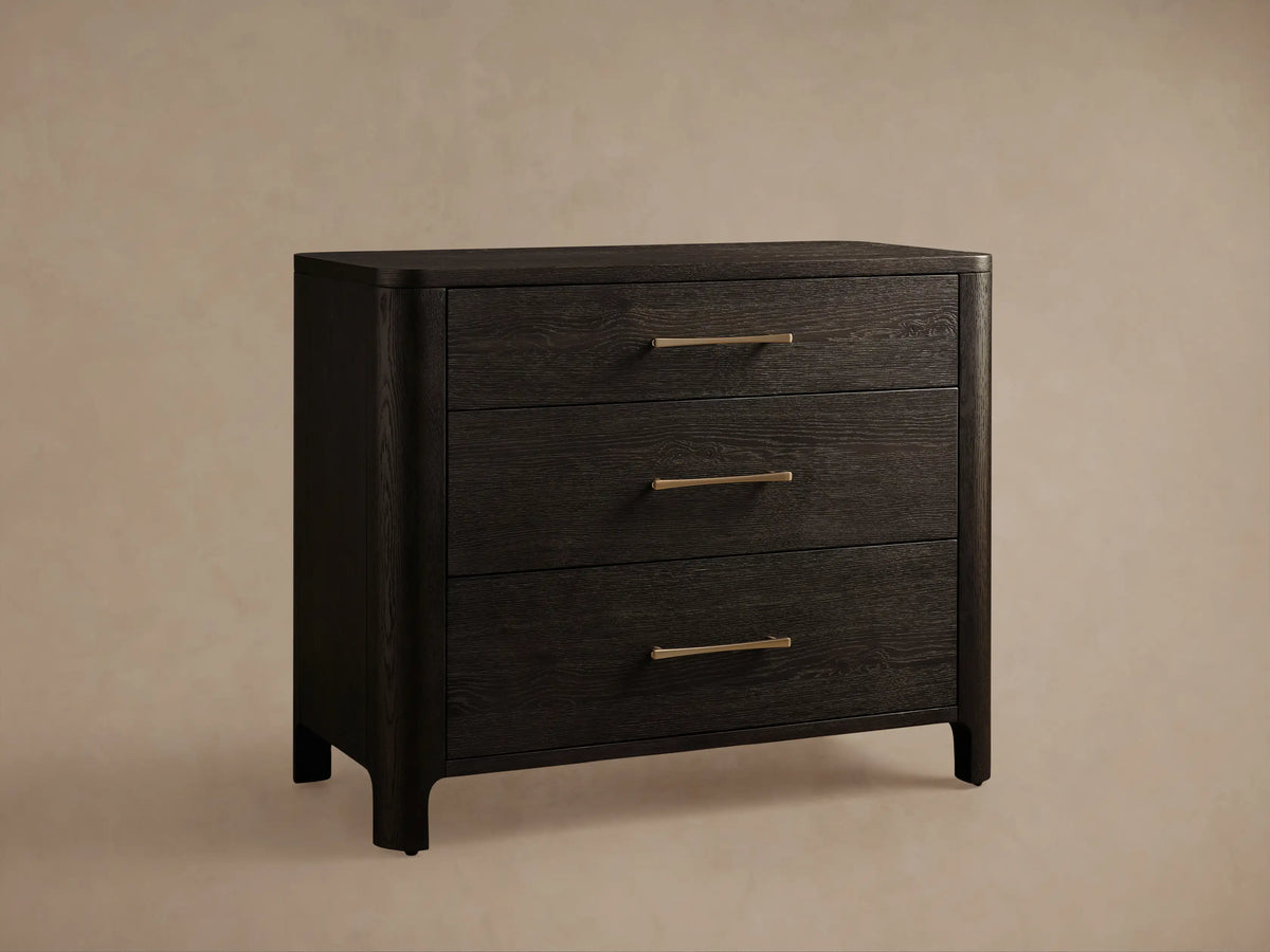 Calista Three-Drawer Chest, dark oak with prominent grain. Upper drawer closed, middle drawer slightly open. Brass bar handles.