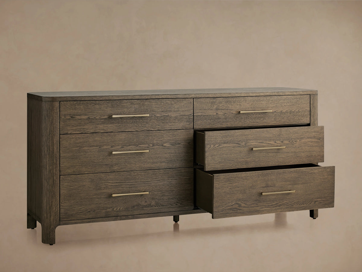 Calista Six-Drawer Dresser in dark veneered oak finish, featuring six drawers with gold handles, two slightly open, against a beige background.