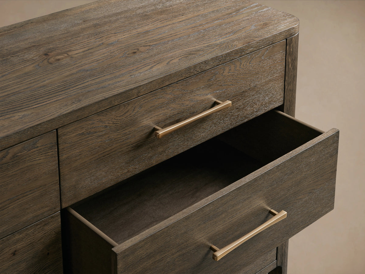 Calista Nine-Drawer Dresser made of veneered oak with a satin sheen, featuring metal handles. Nine drawers in three rows. Wood grain visible.