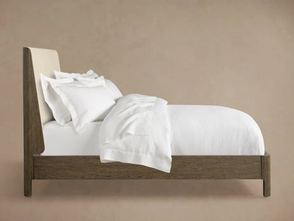 Close-up of the light cream upholstered headboard of the Calista Bed, featuring a woven texture and dark veneered oak frame.