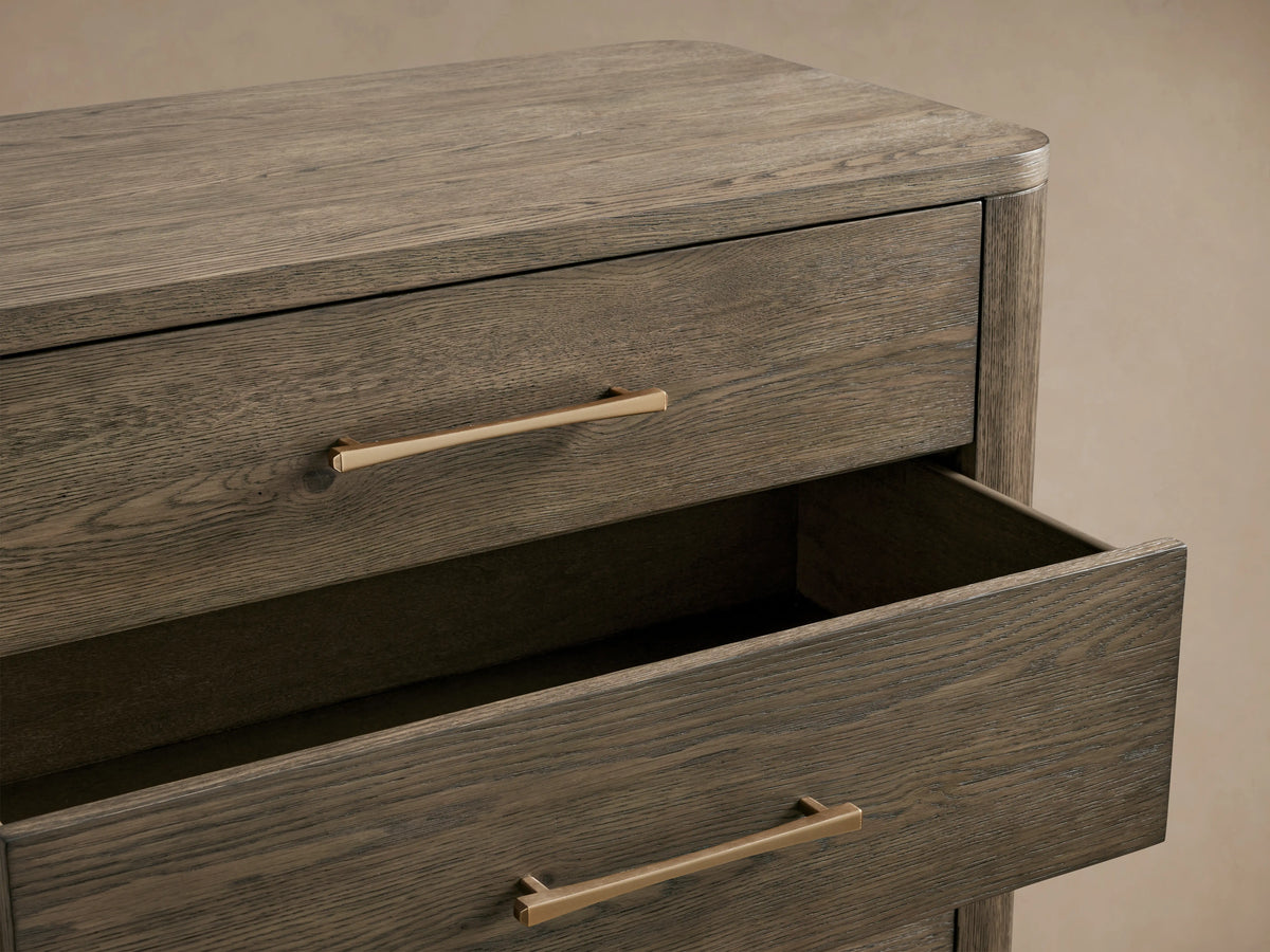 Calista Five-Drawer Dresser in veneered oak with brass handles. Upper drawer is slightly open, showcasing textured wood finish.