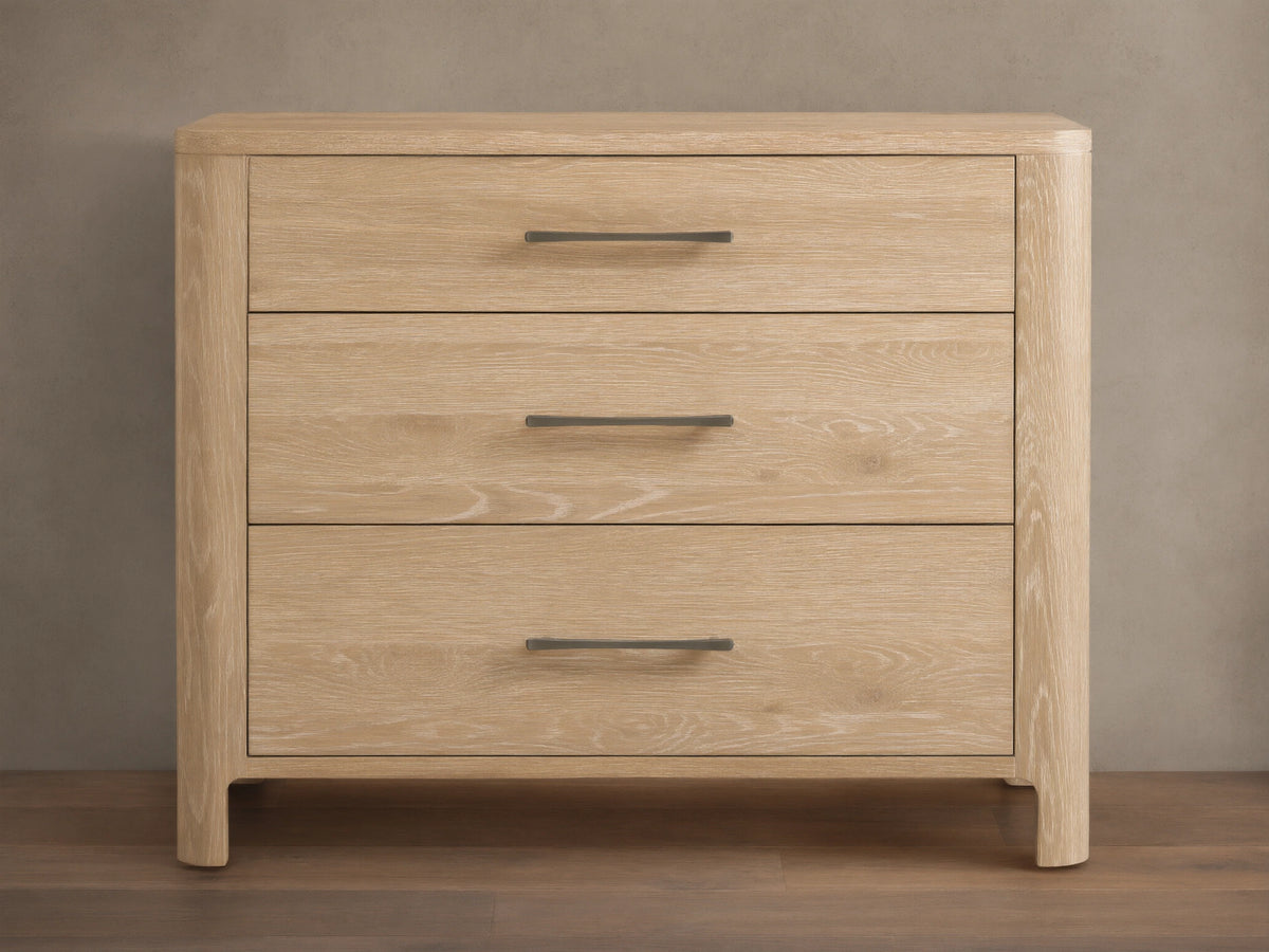 Calista Three-Drawer Chest made of light oak with natural wood grain, featuring three drawers and dark horizontal handles, against a wall.