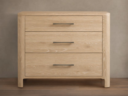 Calista Three-Drawer Chest made of light oak with natural wood grain, featuring three drawers and dark horizontal handles, against a wall.