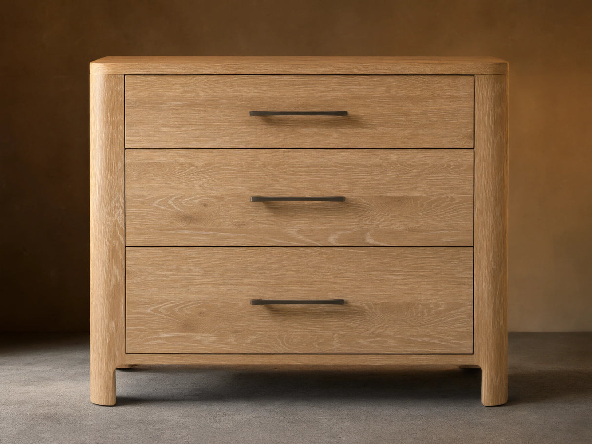 Calista Three-Drawer Chest made of light oak with natural wood grain, featuring three drawers and dark horizontal handles, against a wall.