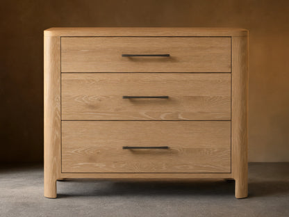 Calista Three-Drawer Chest made of light oak with natural wood grain, featuring three drawers and dark horizontal handles, against a wall.
