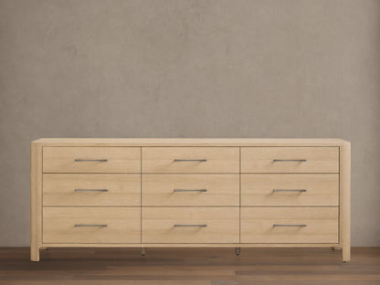 Calista Nine-Drawer Dresser: light oak wood with rounded edges. Features nine drawers with horizontal matte silver bar pulls. Front view.