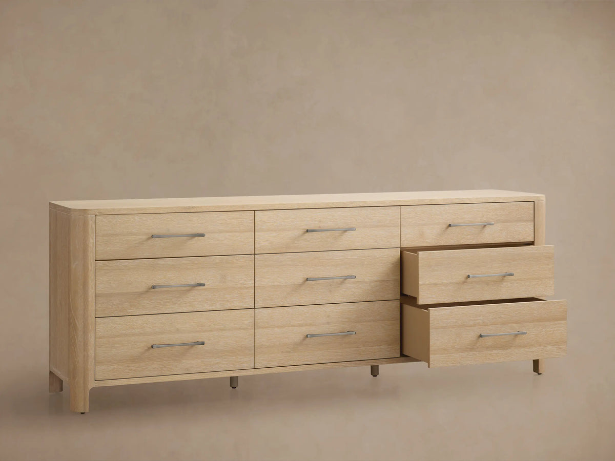 Calista Nine-Drawer Dresser: light oak wood with rounded edges. Features nine drawers with horizontal matte silver bar pulls. Front view.