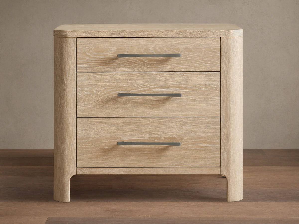 Calista Closed Nightstand in light oak wood with prominent grain, featuring rounded edges and three drawers with gray pull handles.