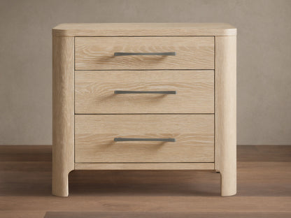 Calista Closed Nightstand in light oak wood with prominent grain, featuring rounded edges and three drawers with gray pull handles.