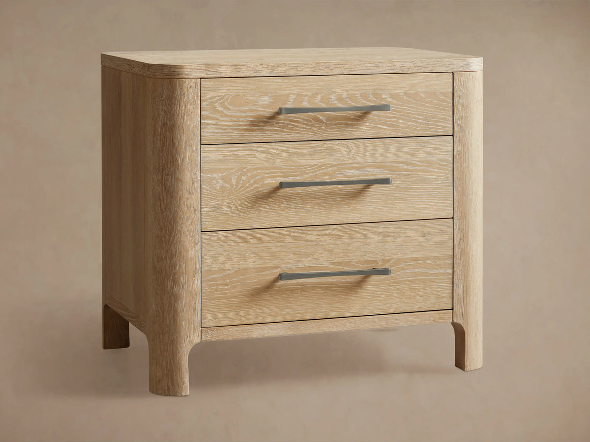 Calista Closed Nightstand in light oak wood with prominent grain, featuring rounded edges and three drawers with gray pull handles.