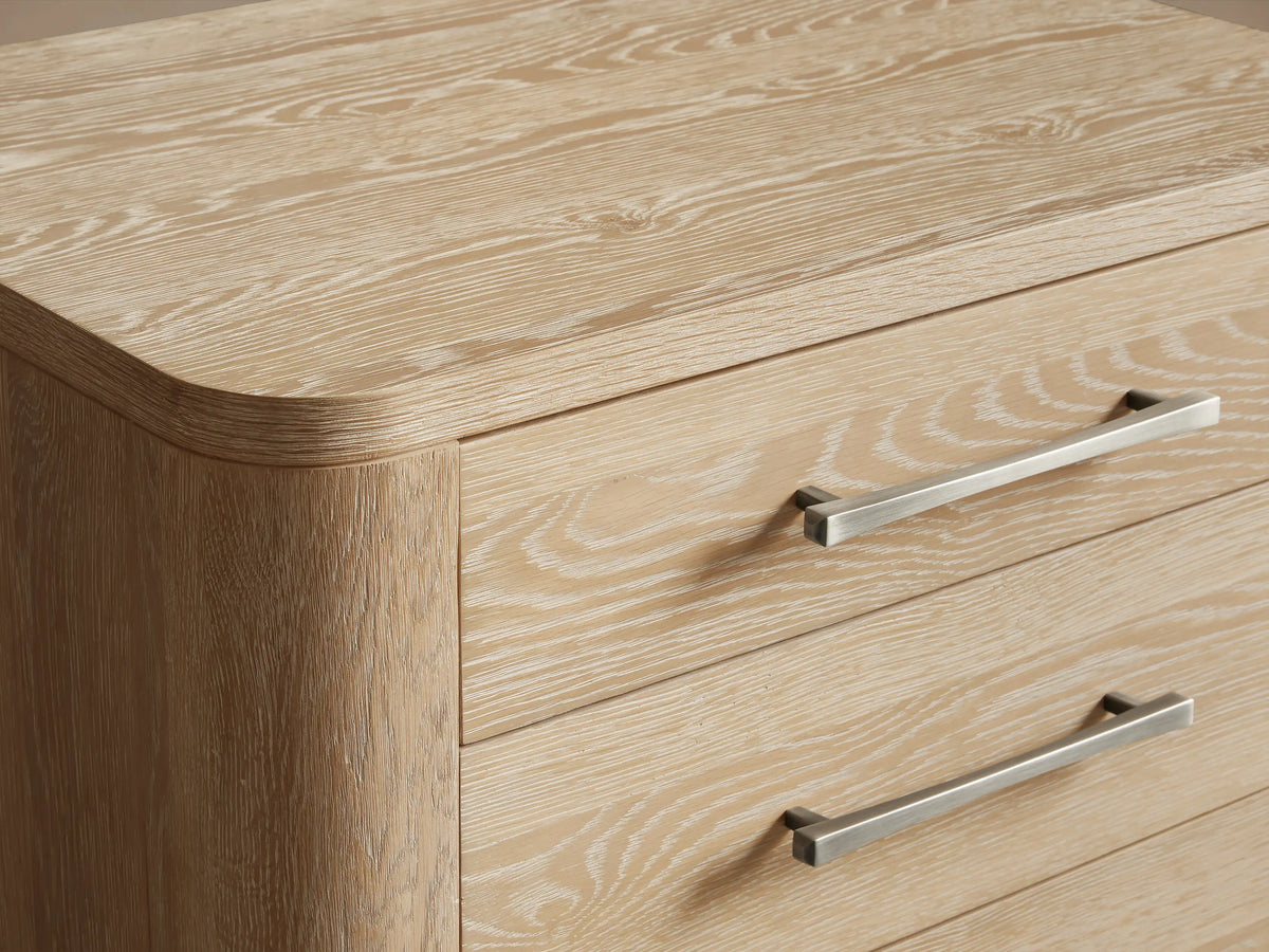 Calista Closed Nightstand, light oak with visible grain, 3 drawers, dark slim pulls, rounded corners & short legs. Front view.
