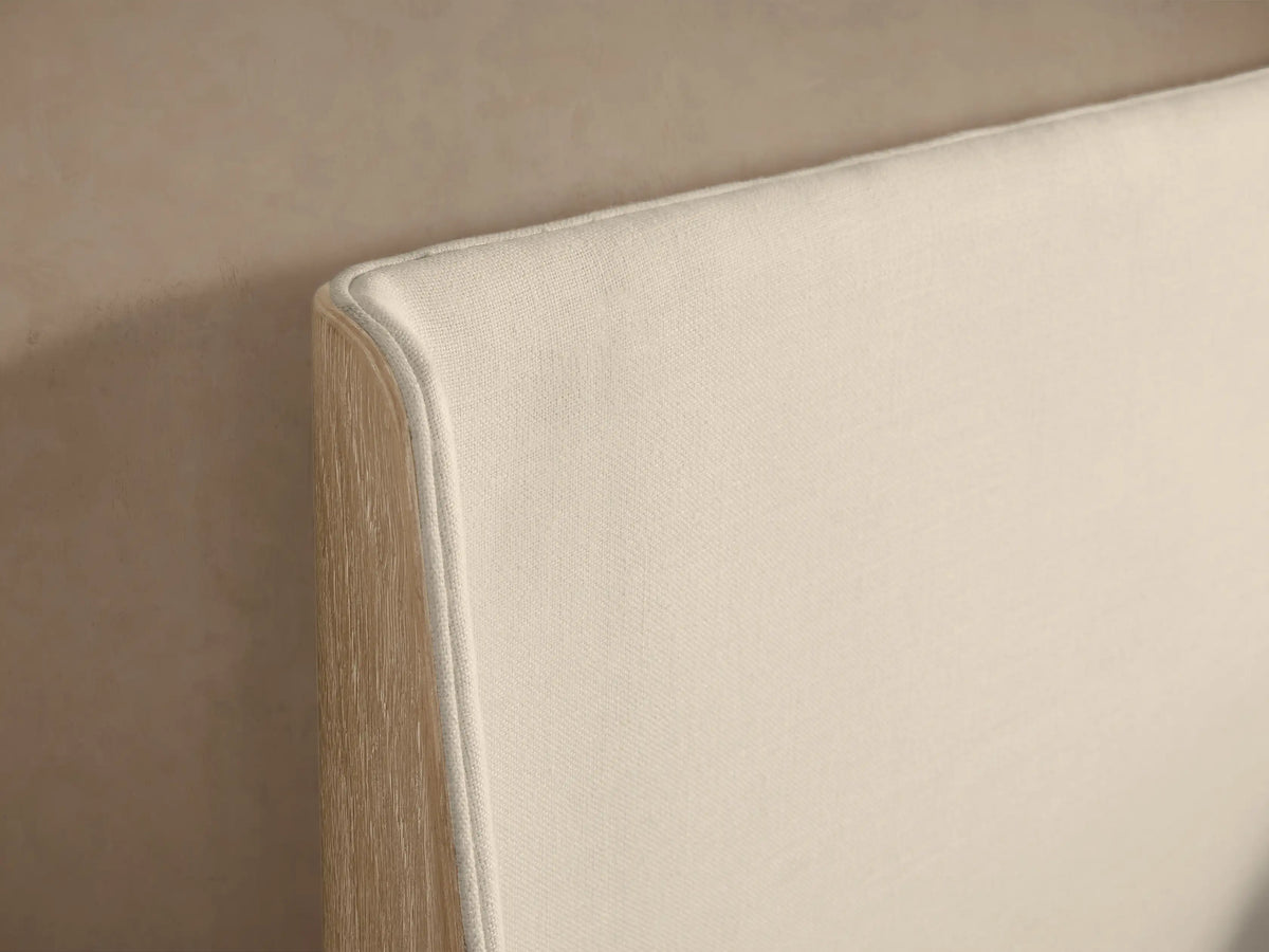Front view of the Calista Bed with a cream upholstered headboard, light wood frame, and white bedding.