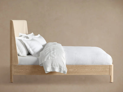 Close-up of the Calista Bed, featuring an off-white upholstered headboard with piping detail and visible light oak frame.