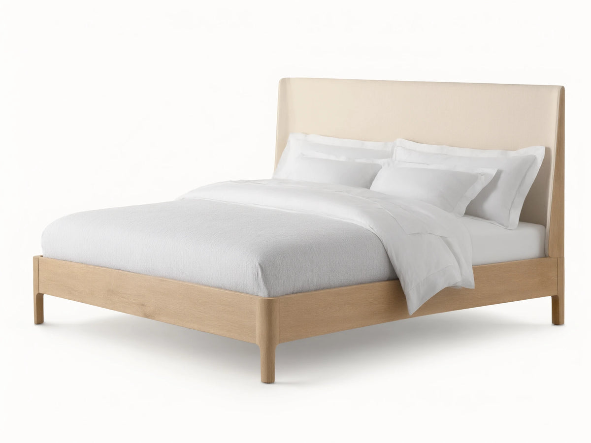 Front view of the Calista Bed, featuring a light oak wood frame and a cream upholstered headboard, dressed with white bedding.