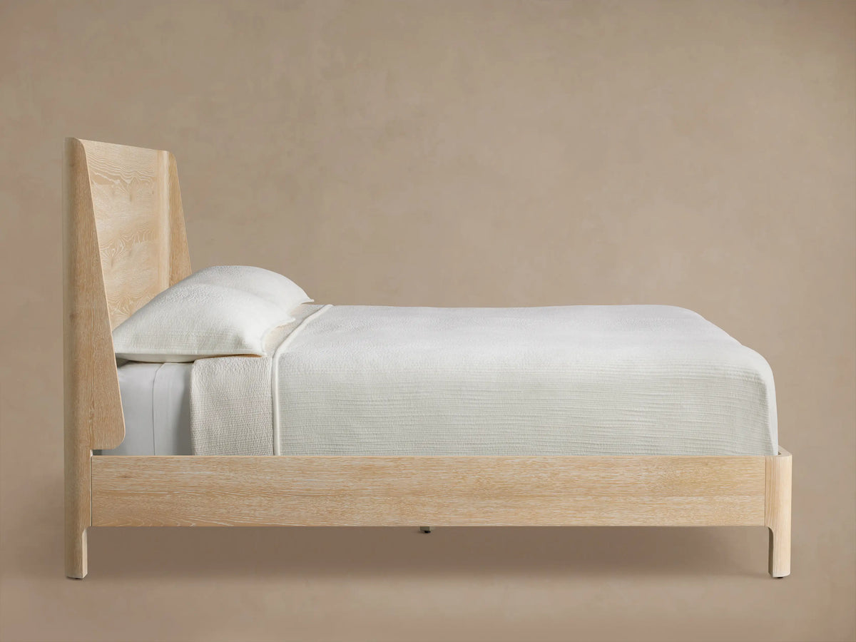 CALISTA WOOD QUEEN BED SAND headboard with a light wood grain pattern, featuring a curved edge against a beige wall.