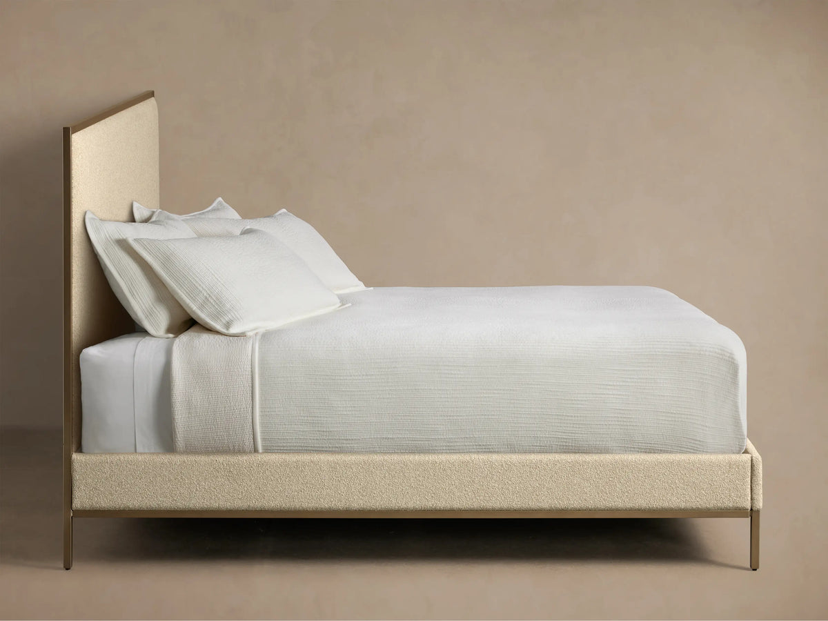 Close-up of the light beige nubby textured fabric panel framed by bronze-toned metal on the Chamberlain Bed headboard.