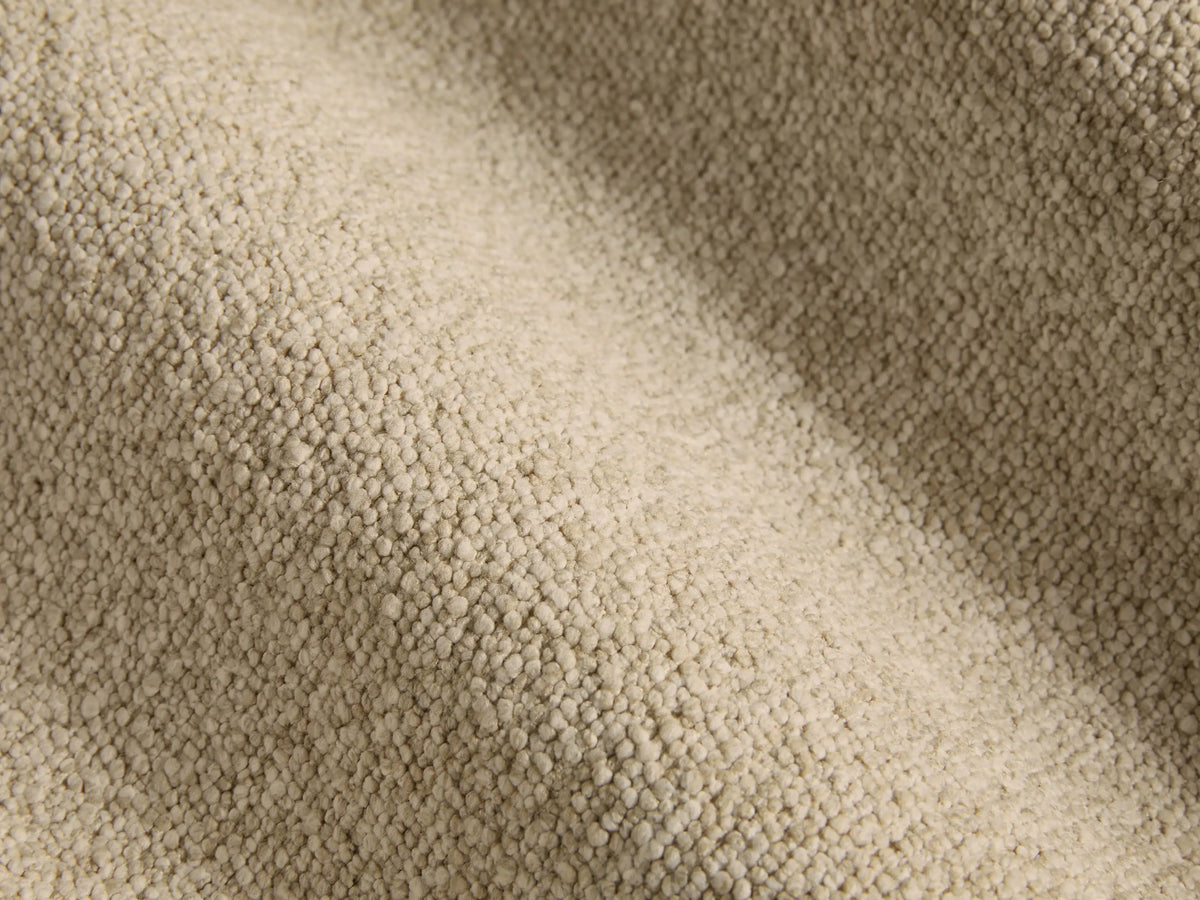 Side profile of the beige upholstered Chamberlain Bed with a metal trim headboard, dressed in white sheets and pillows.