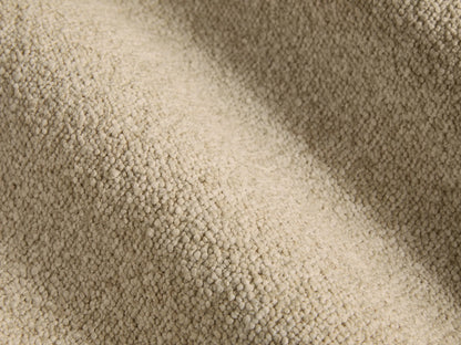 Side profile of the beige upholstered Chamberlain Bed with a metal trim headboard, dressed in white sheets and pillows.