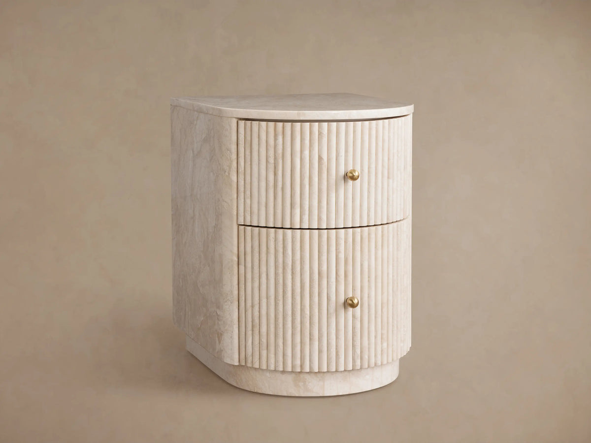 Close-up Clementine Reeded Stone Nightstand. Creamy stone with reeded texture, brass pulls. Bottom drawer partially open.