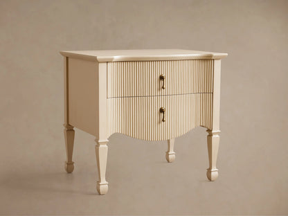 Cream Conrad Nightstand with reeded facade, 2 drawers, antique brass pulls, and curved base. Tapered legs on wood floor.