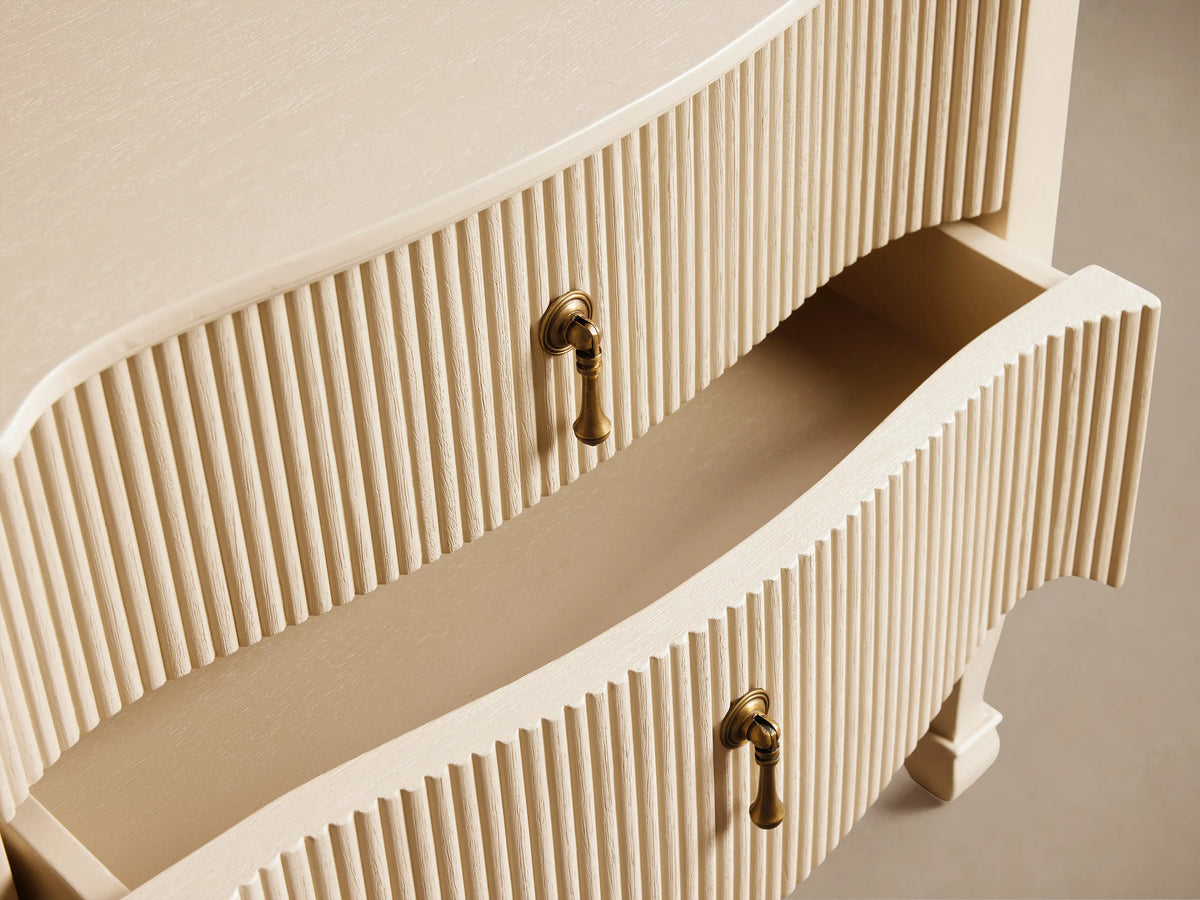 Light cream Conrad Nightstand, 2 reeded drawers with antique brass pendant pulls, scalloped bottom edge, and tapered legs.