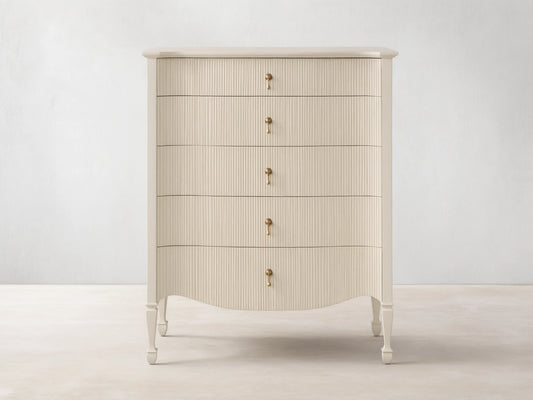 Conrad Five-Drawer Dresser, light cream, reeded fronts, 5 antique brass pendant pulls, curved base, on wooden floor.