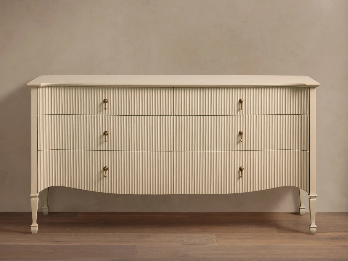 Conrad Six-Drawer Dresser, cream-colored with reeded texture, antique brass pendant pulls, elegant curved bottom, and tapered legs.