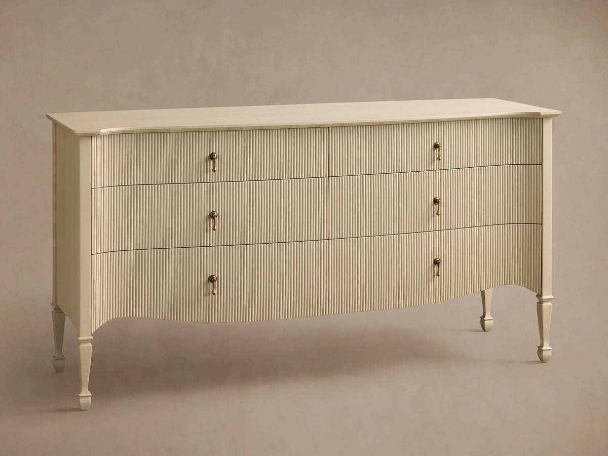 Conrad Six-Drawer Dresser, cream-colored with reeded texture, antique brass pendant pulls, elegant curved bottom, and tapered legs.