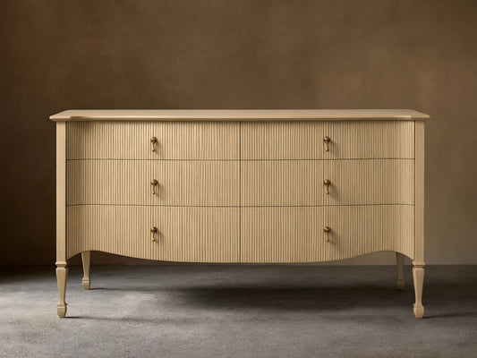 Conrad Six-Drawer Dresser, cream-colored with reeded texture, antique brass pendant pulls, elegant curved bottom, and tapered legs.