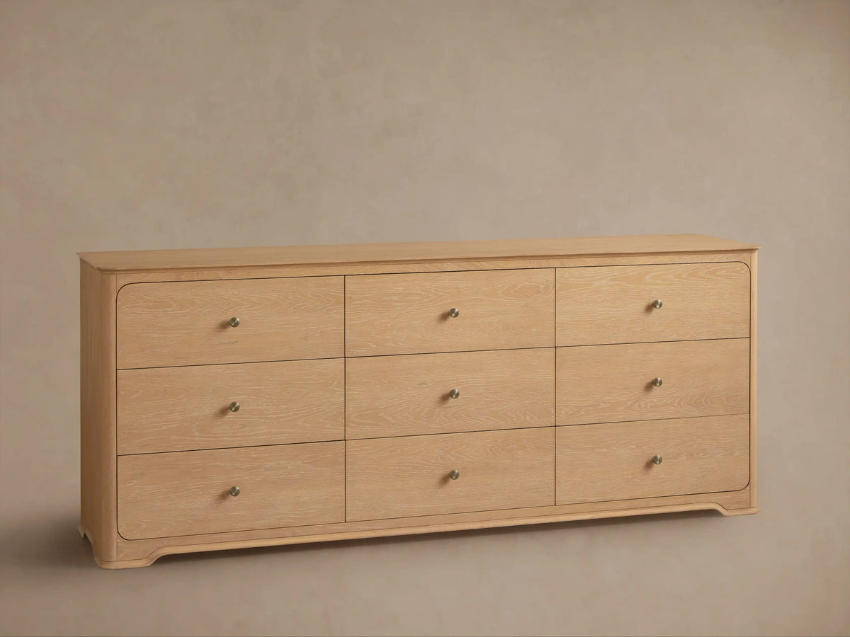 Conley Nine-Drawer Dresser: Light oak wood with 9 drawers, champagne brass pulls, rounded corners, subtle curved base.