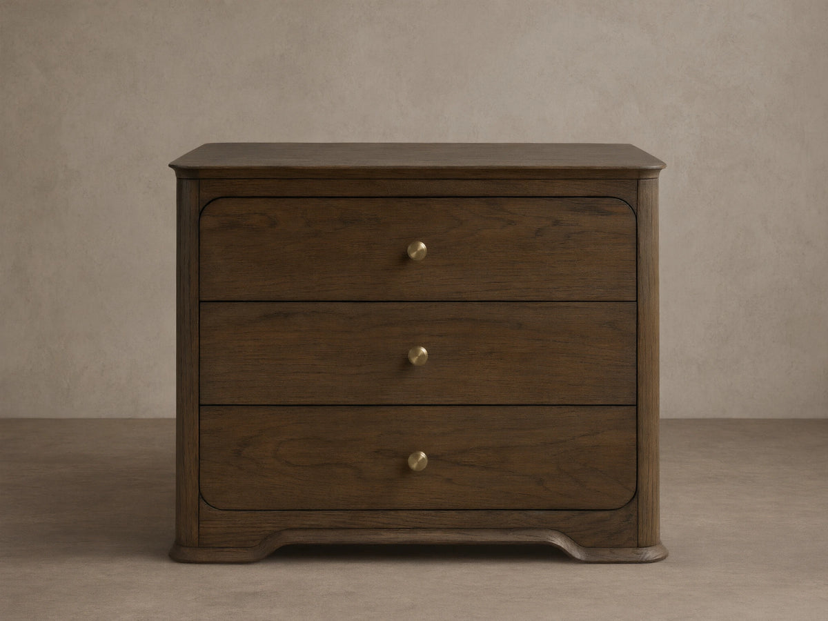 Dark oak Conley Nightstand with three drawers, champagne brass pulls, curved edges, and a sculpted base, shown front on.