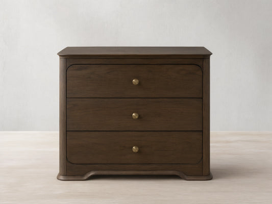 Dark oak Conley Nightstand with three drawers, champagne brass pulls, curved edges, and a sculpted base, shown front on.