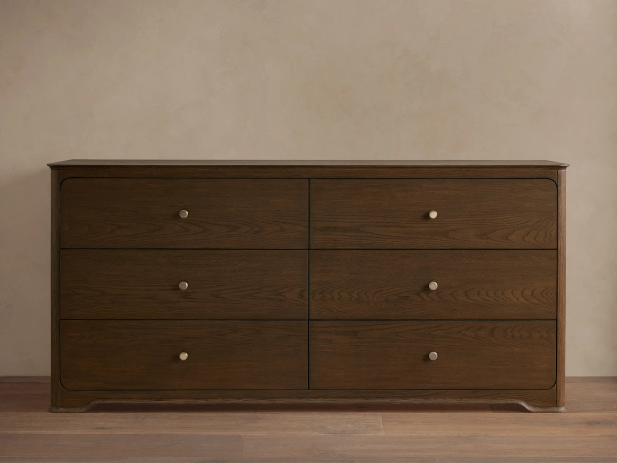 Conley Six-Drawer Dresser made of dark oak with visible wood grain, soft rounded edges & champagne brass knobs.