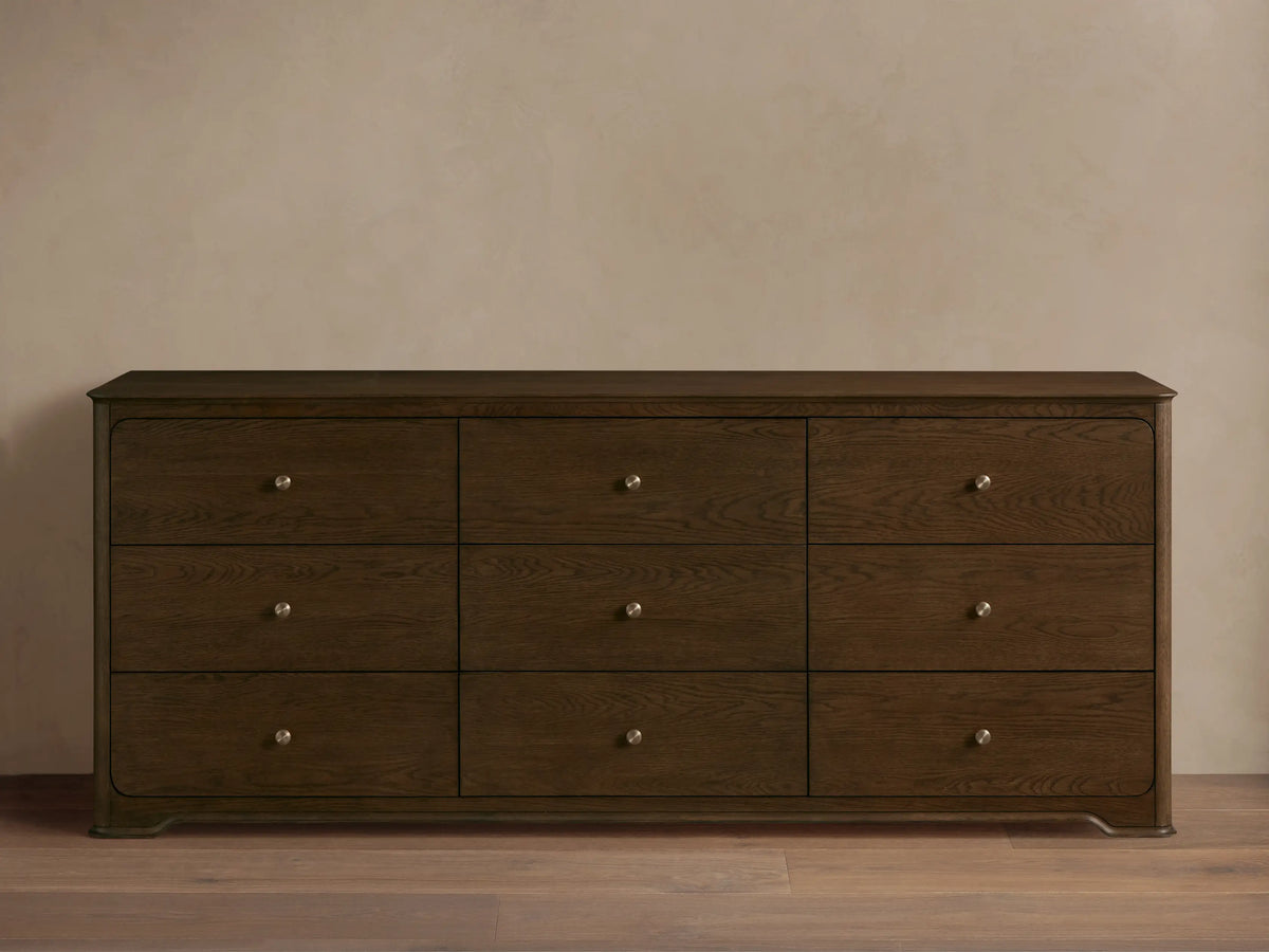 Conley Nine-Drawer Dresser: Dark brown oak wood, 9 drawers with visible grain and champagne brass pulls, against a beige wall.