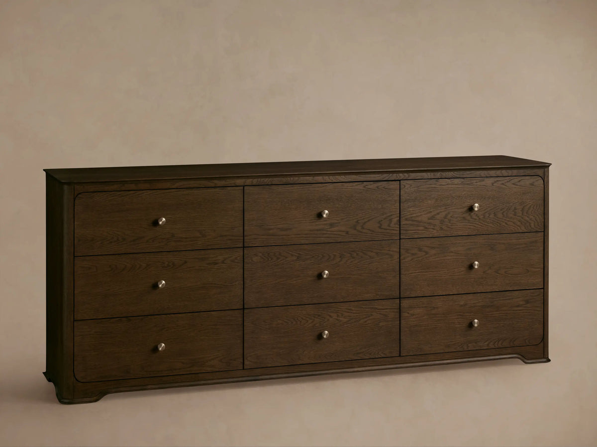 Conley Nine-Drawer Dresser: Dark brown oak wood, 9 drawers with visible grain and champagne brass pulls, against a beige wall.
