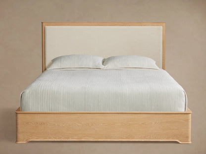 Conley Panel Bed: light oak frame, cream upholstered headboard, white textured bedding, on a wood floor, angled right.
