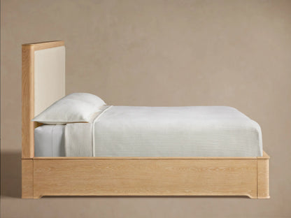 Conley Panel Bed: Close-up of light oak wood headboard. Curved frame with prominent grain borders textured off-white fabric.