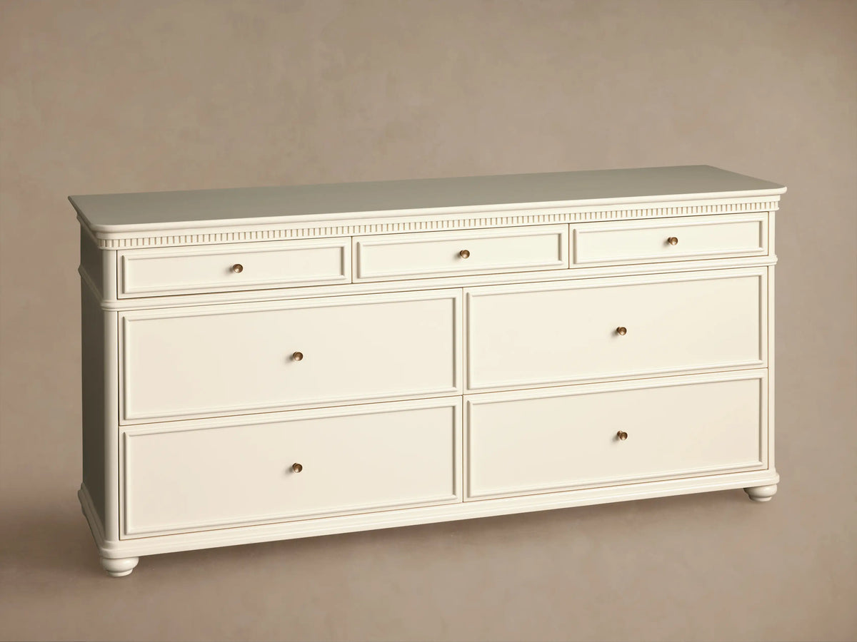 Cr??me finished Carlisle dresser with fluted top molding, 7 drawers, and antique brass knobs on wood floor.