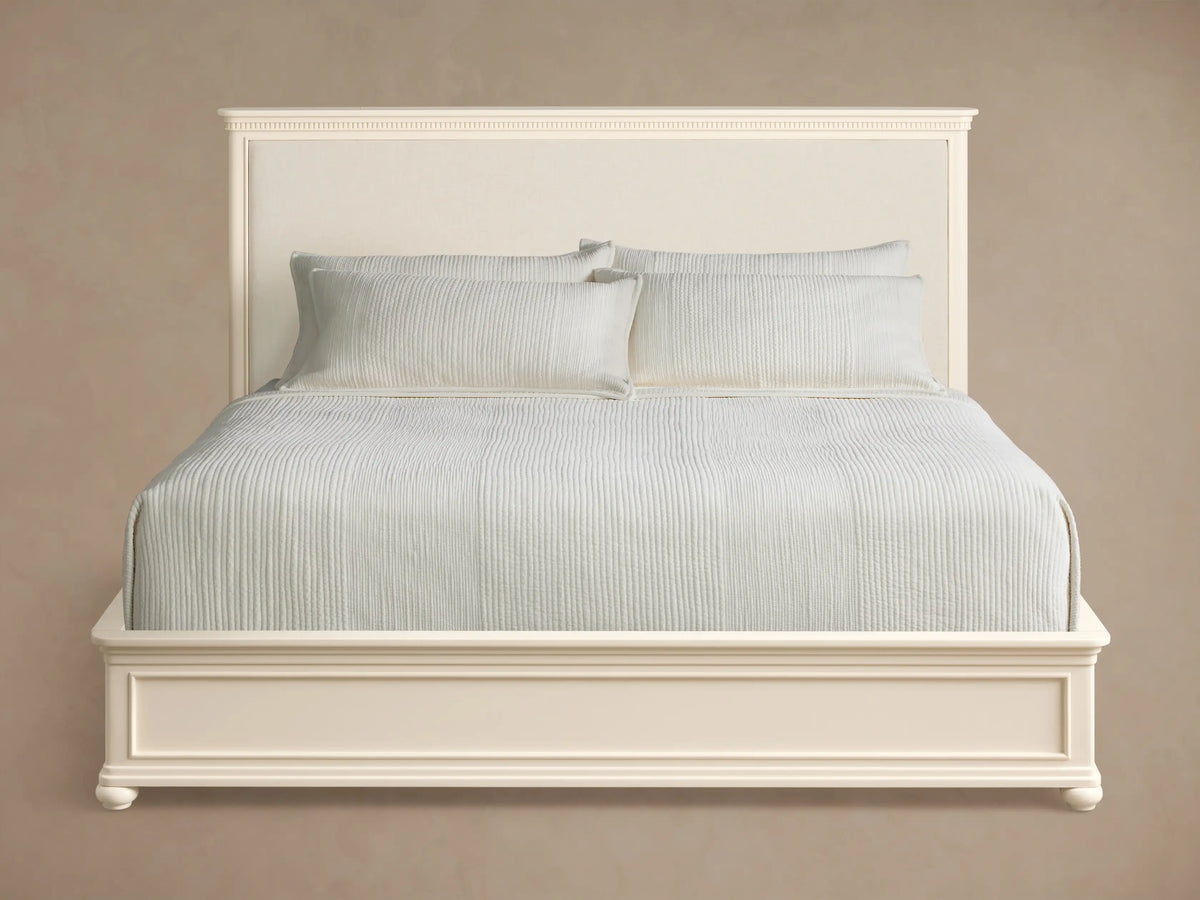 Carlisle Bed with a crv®me-finished frame, upholstered headboard, and light grey bedding, shown from an angle on a wooden floor.