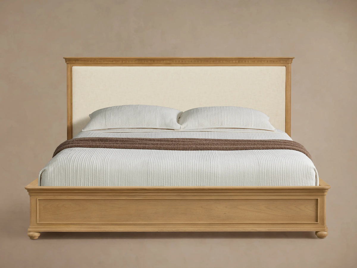 Carlisle Bed: Light oak frame, cream upholstered headboard, white striped bedding, brown throw, on wood floor.
