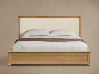 Carlisle Bed: Light oak frame, cream upholstered headboard, white striped bedding, brown throw, on wood floor.