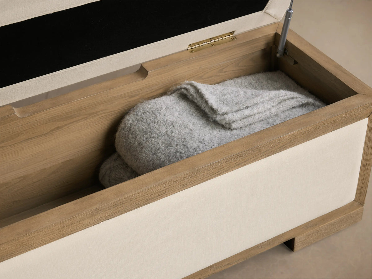 Front view of the cream Darien Storage Bench with light oak wood frame, upholstered top and side panels.